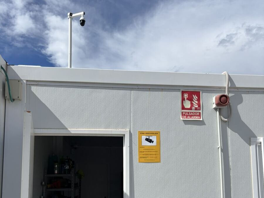 Yellow video-surveillance notice beside the door of a site office, with a camera on a mast above the roof